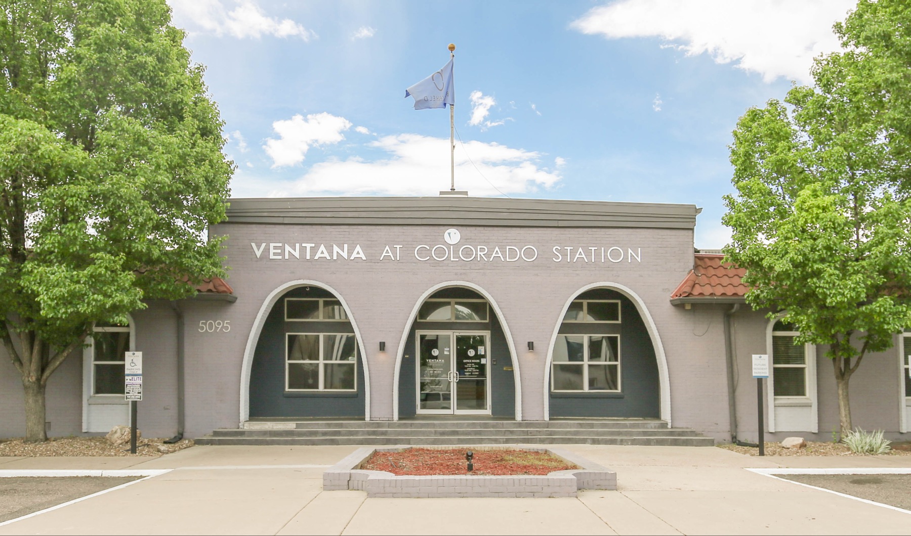 Apartment leasing office exterior with arches and trees